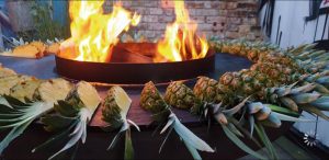 Um ein offenes Feuer herum sind auf einer schwarzen Platte Ananasviertel aufgereiht