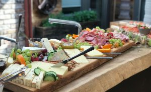 Aufschnittplatte mit verschiedenen Sorten Käse und Wurst, darunter Schnittkäse, Weichkäse, Salami und Schinken. Angerichtet auf einer rustikalen Holzplatte.